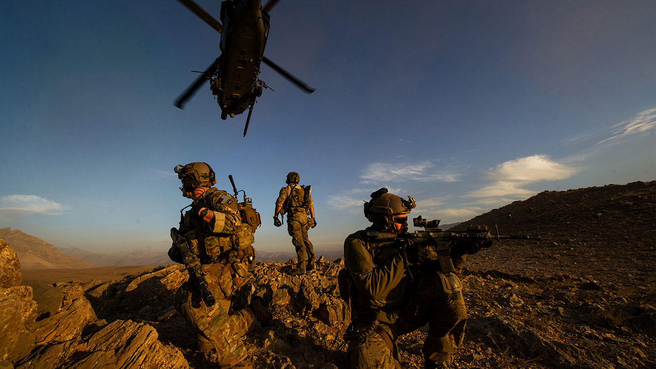 Special Operations Airmen navigating the land with a helicopter hovering over them.